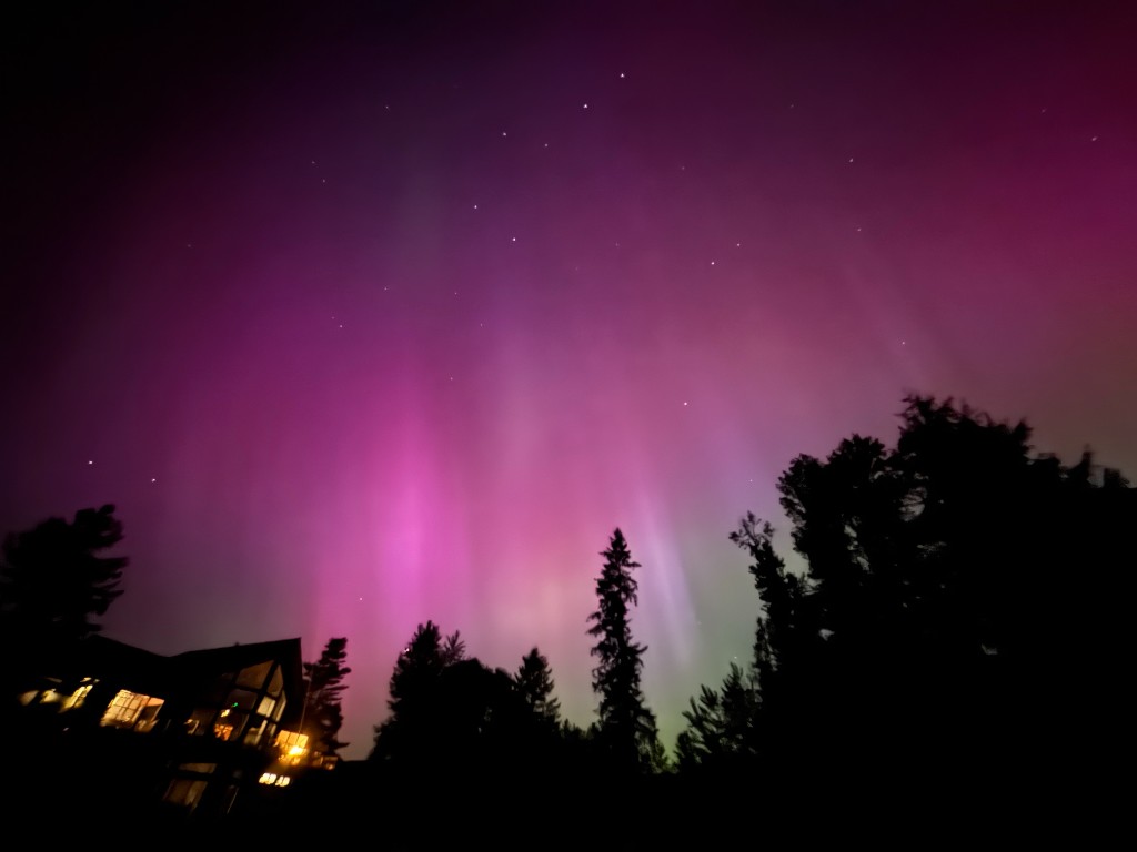 Aurora borealis northern lights glowing pink and violet over Lewis River Estate property house and treeline in Woodland Washington near Portland Oregon
