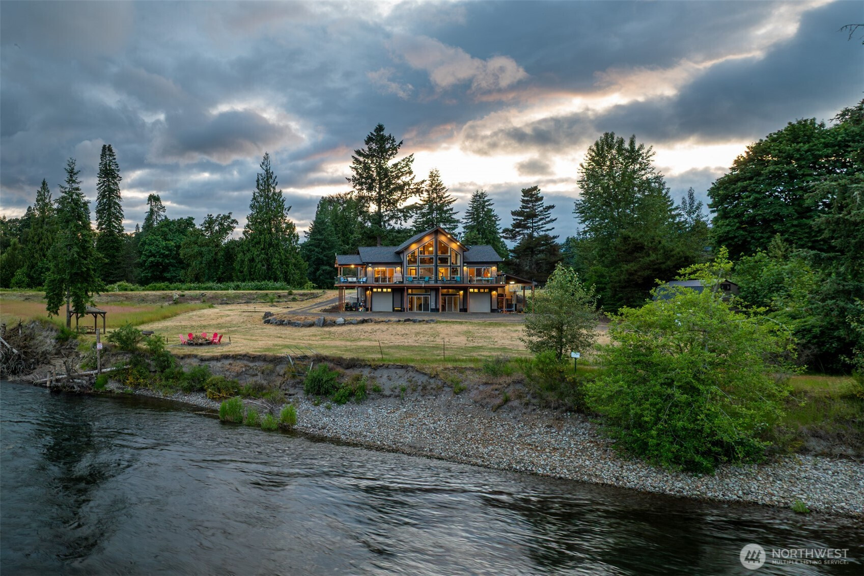 Lewis River Estate & Gardens at dusk — riverside lawn, fire pit, and main estate with the Lewis River in the foreground