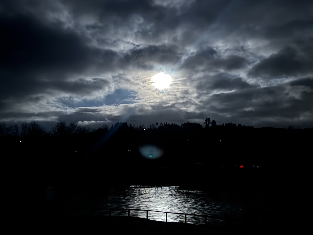 Full moon breaking through dramatic clouds over Lewis River with moonlight reflecting on water at Lewis River Estate Woodland Washington